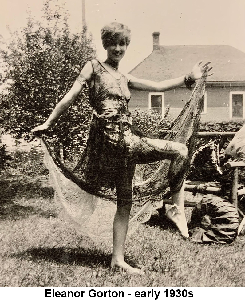 Sepia-tone photo of Eleanor Gorton smiling with bobbed hair, wearing a diaphanous slinky dress, standing barefoot with one knee lifted, on the lawn behind a house, holding up the long trains of the dress with both hands.
